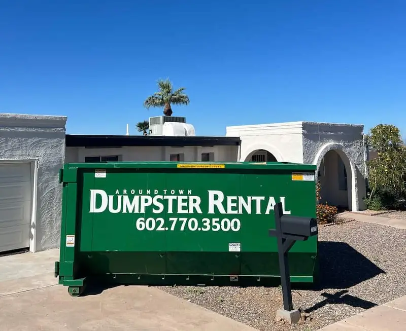 Green Around Town roll-off dumpster at a white home with a palm tree