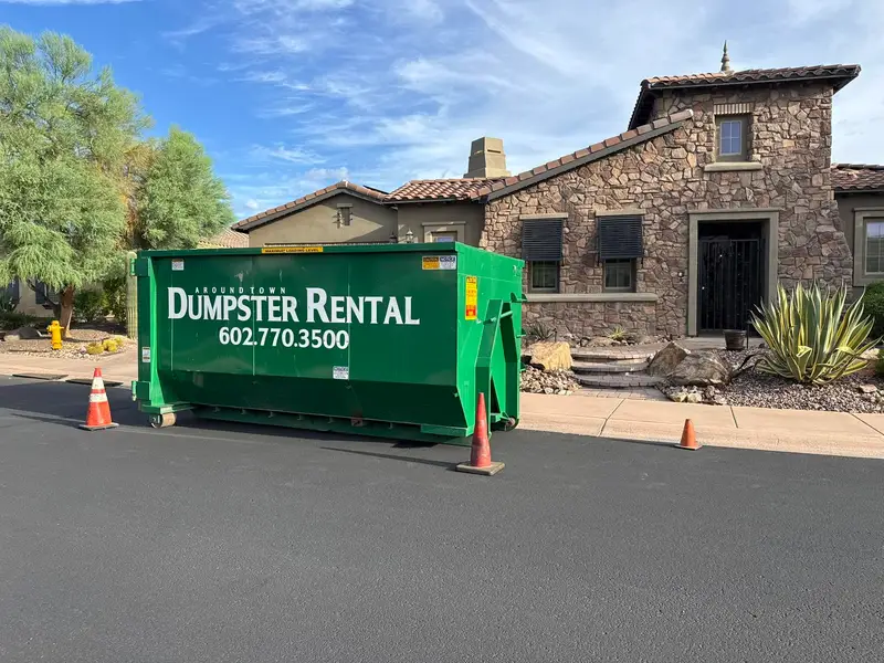 Green Around Town roll-off dumpster on a residential driveway in front of a stone home